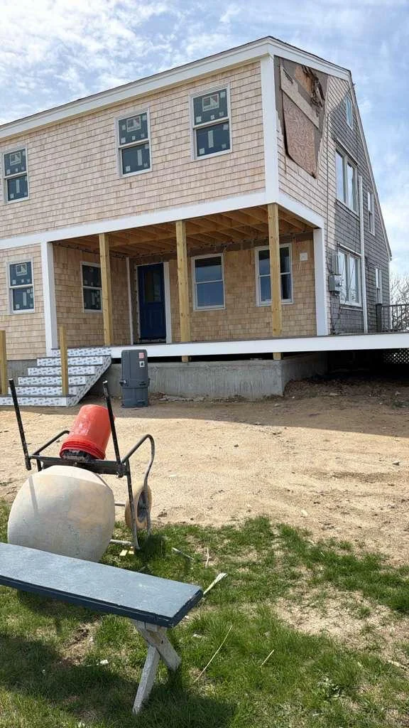 Foundation and porch work beside a cedar-shingle home